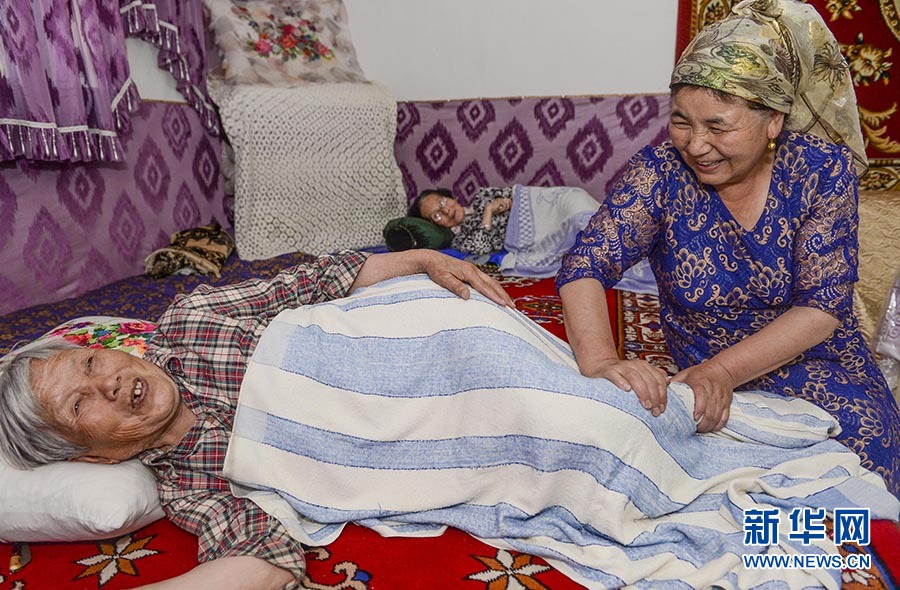 新华社照片，乌鲁木齐，2016年6月15日 新疆：沙尼汗大妈的“老人俱乐部” 在沙尼汗居家养老点，沙尼汗（右）在照顾83岁的黄建国老人午休，并帮她按摩双腿（6月3日摄）。平时，沙尼汗对孤身一人居住的黄建国格外关照，还称呼其为“妈妈”。 包粽子、蒸抓饭、洗水果、打牌下棋……位于新疆阜康市阜新街道文化路社区的“老人俱乐部”里充满欢声笑语，宛如一个大家庭。今年54岁的沙尼汗·艾塔木经营着“老人俱乐部”，吸引了周围的老人前来作客，也让30多位各民族老人在这里安度晚年。 善良热心的沙尼汗大妈一直以来不仅孝敬公婆，还帮助周围的独居老人做饭、洗衣，陪他们聊天，她家冬暖夏凉的小院也成了老人们最爱去的地方。2010年的一天，社区书记找到沙尼汗，希望她能将社区里因子女不在身边、生活需要照顾的老年人集中到她家，成立家庭式居家养老服务点。当年末，新疆首个家庭式居家养老服务点在沙尼汗家挂牌。5年多来，沙尼汗先后照顾36位汉、回、哈萨克、维吾尔族老人，他们中年龄最大的90多岁，最小的也快60岁。“我喜欢跟老人们在一起，觉得他们就像我自己的父母亲和兄弟姐妹一样，感情太深了！”脸上始终挂着微笑的沙尼汗动情地说。 沙尼汗的善行得到了社会各界的关注，她先后荣获“全国孝亲敬老之星”“民族团结模范”等称号。在她的影响和带动下，越来越多的志愿者自发来到她家小院为老人们服务。今年3月，阜康市“情暖空巢”沙尼汗居家养老点还成为“全国百佳志愿服务项目”。 新华社记者王菲摄